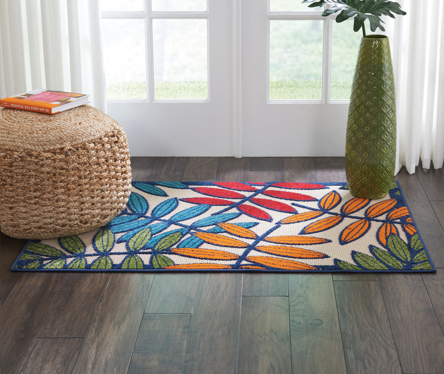 Woven cotton runner rug with blue, green and orange tropical leaves on white, dark blue border, in a bright doorway.