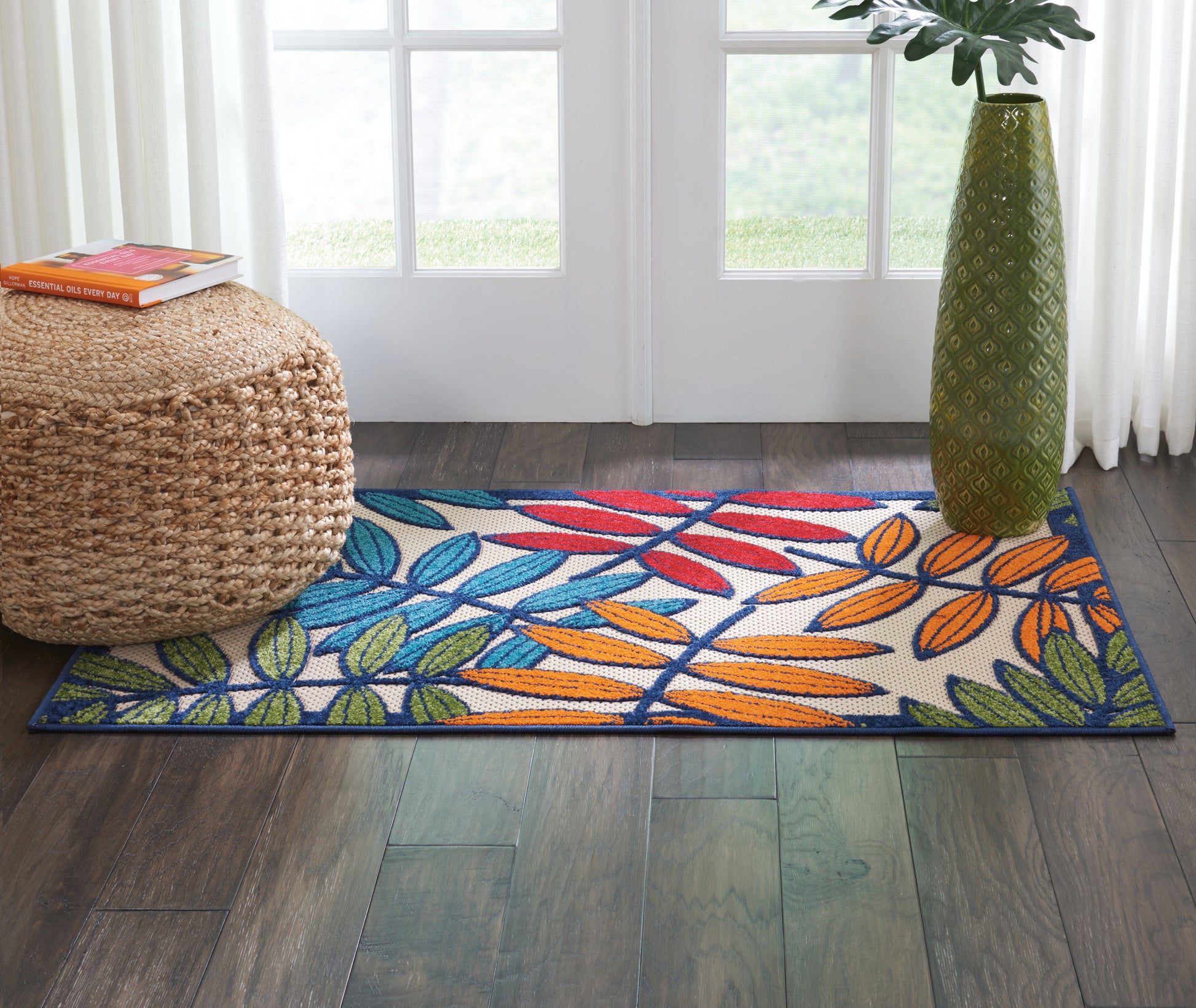 Woven cotton runner rug with blue, green and orange tropical leaves on white, dark blue border, in a bright doorway.