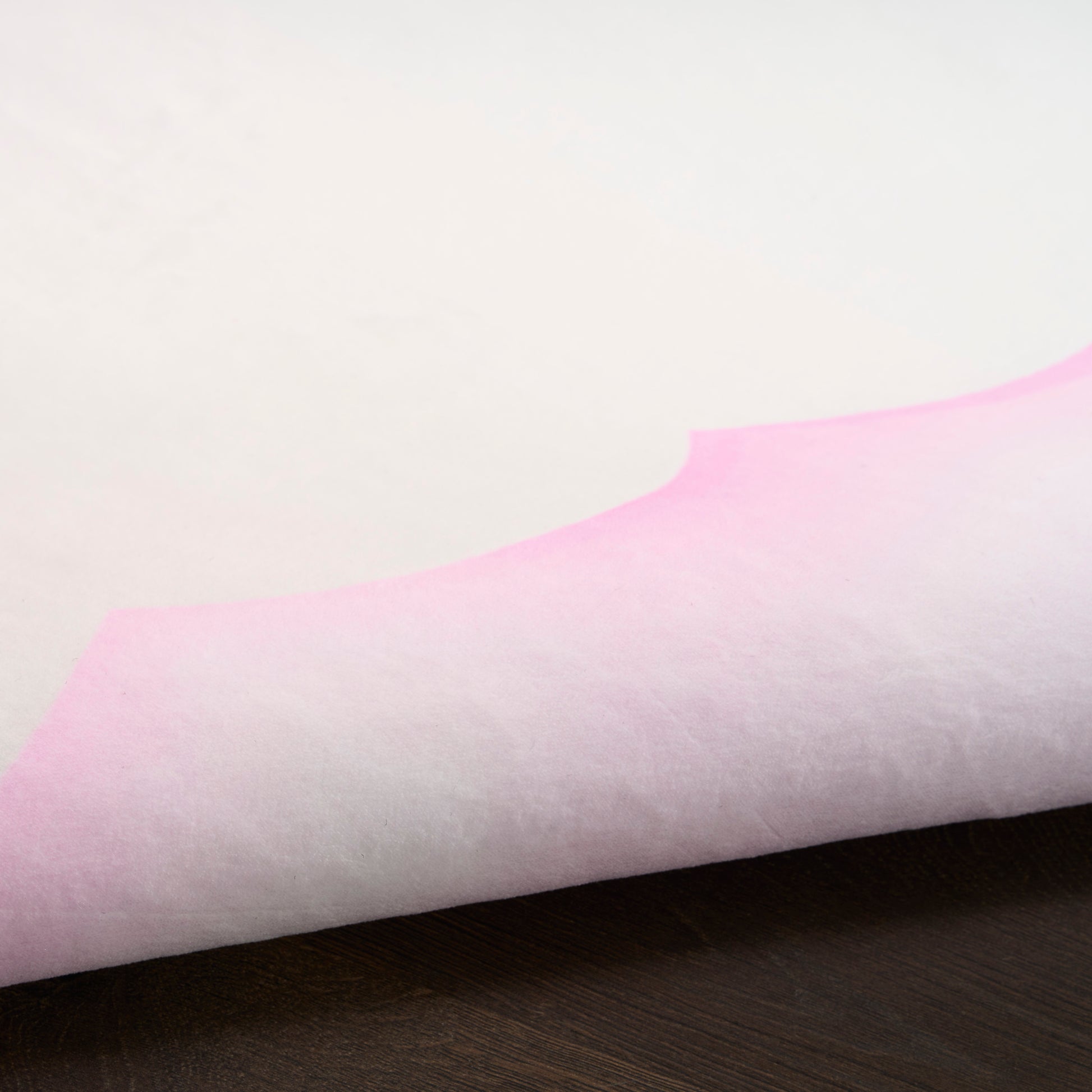White tissue paper with pink gradient curved edge, folded over a dark wooden surface.