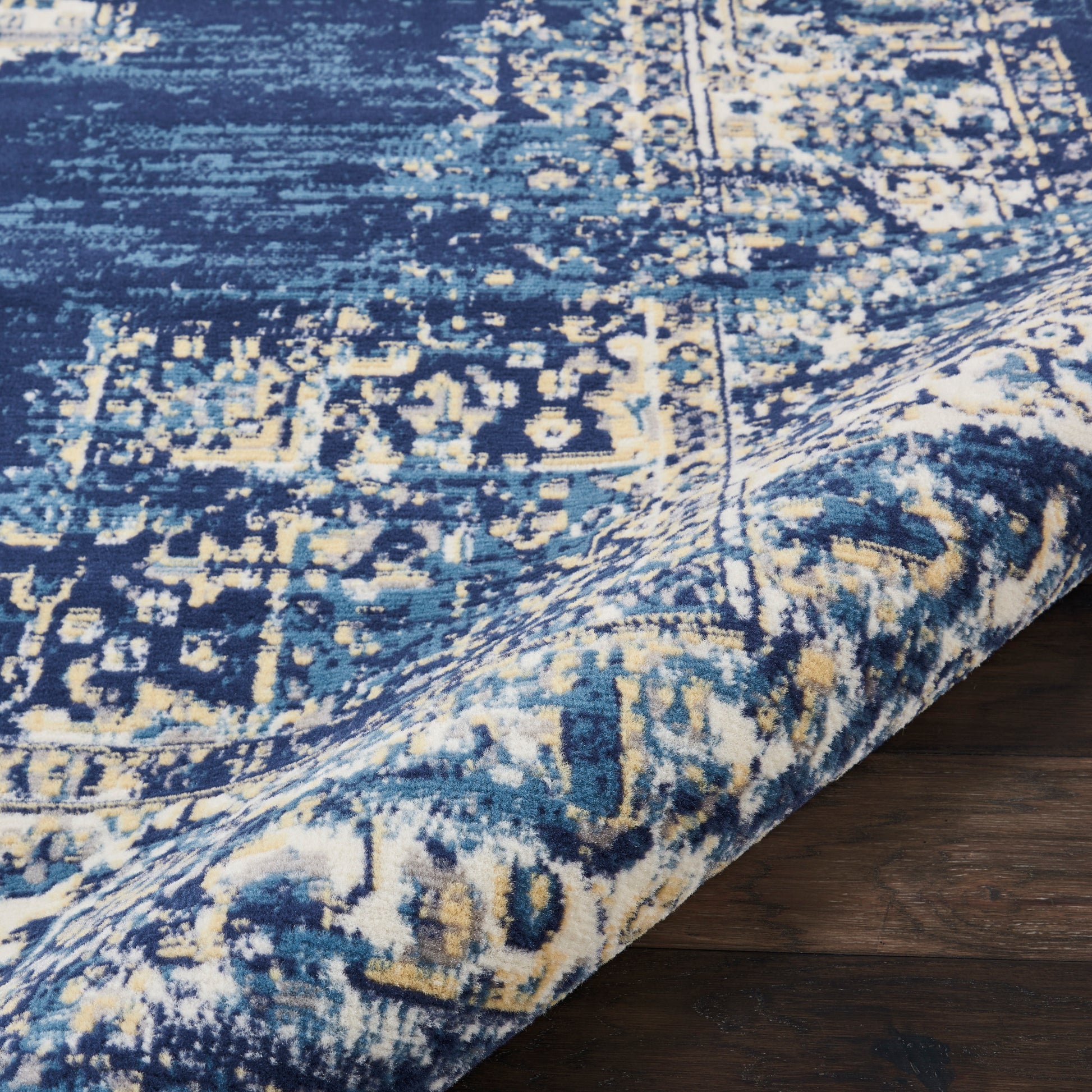 Blue and ivory distressed oriental rug with intricate geometric pattern, measuring 3' x 5', partially rolled on a dark wood floor.