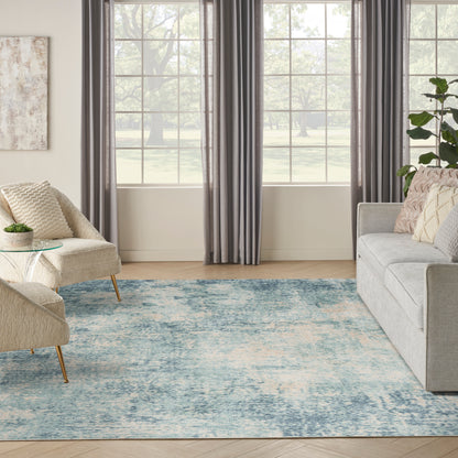 Cozy living room with light gray sofa, beige chairs, blue area rug, glass coffee table, gray curtains, potted plant.
