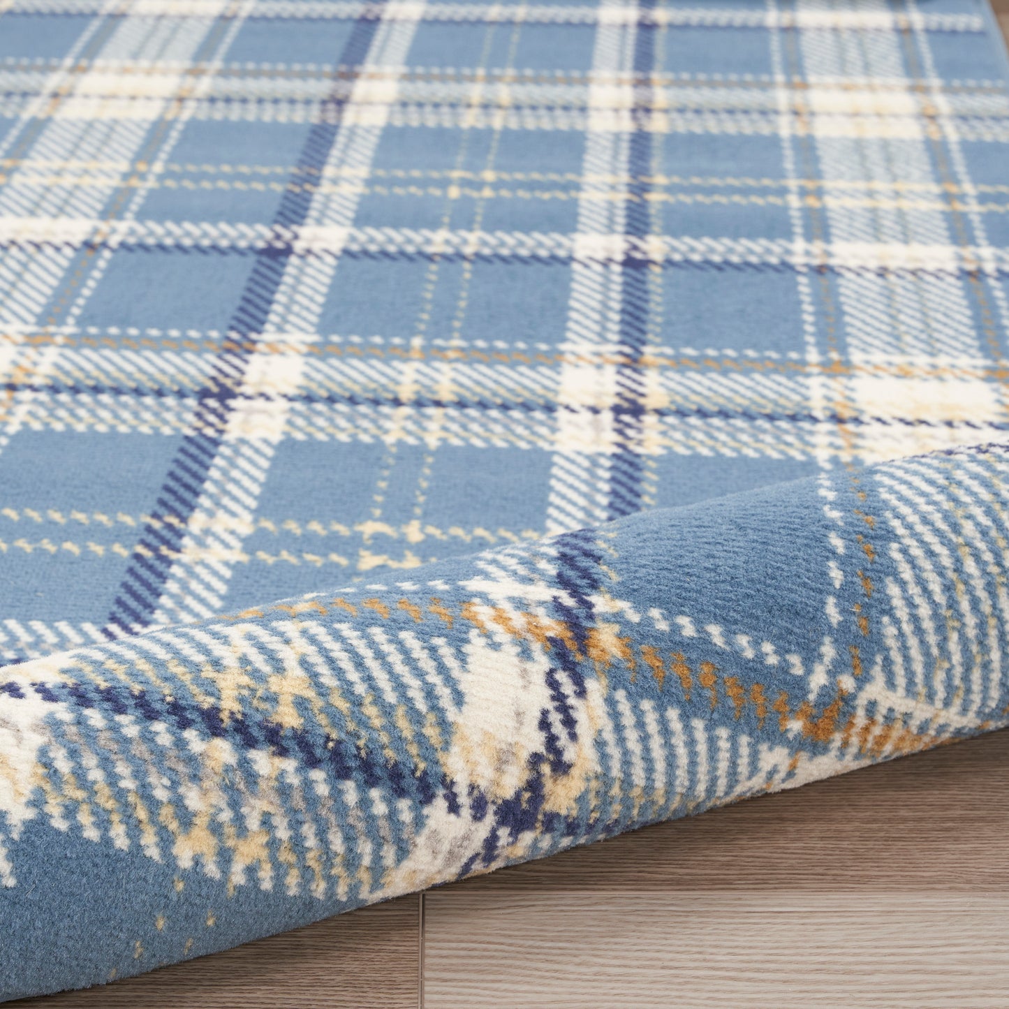 Blue plaid rug with white and tan lines, soft wool-blend texture, laid on light wooden floor with folded corner.
