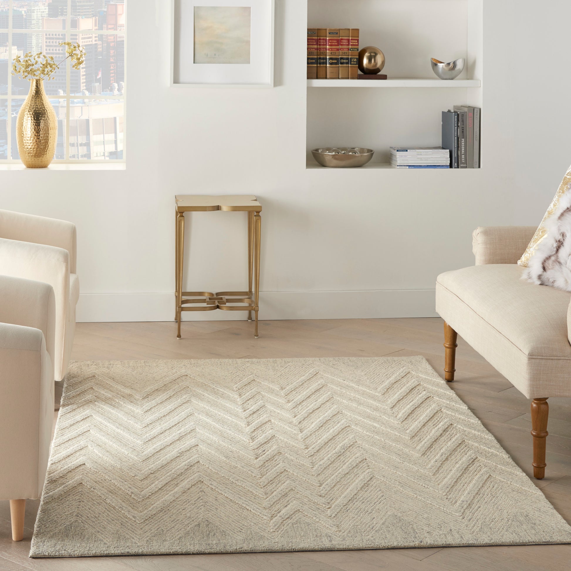 Light beige chevron area rug anchors a bright living room with cream sofas and white built-in shelving.
