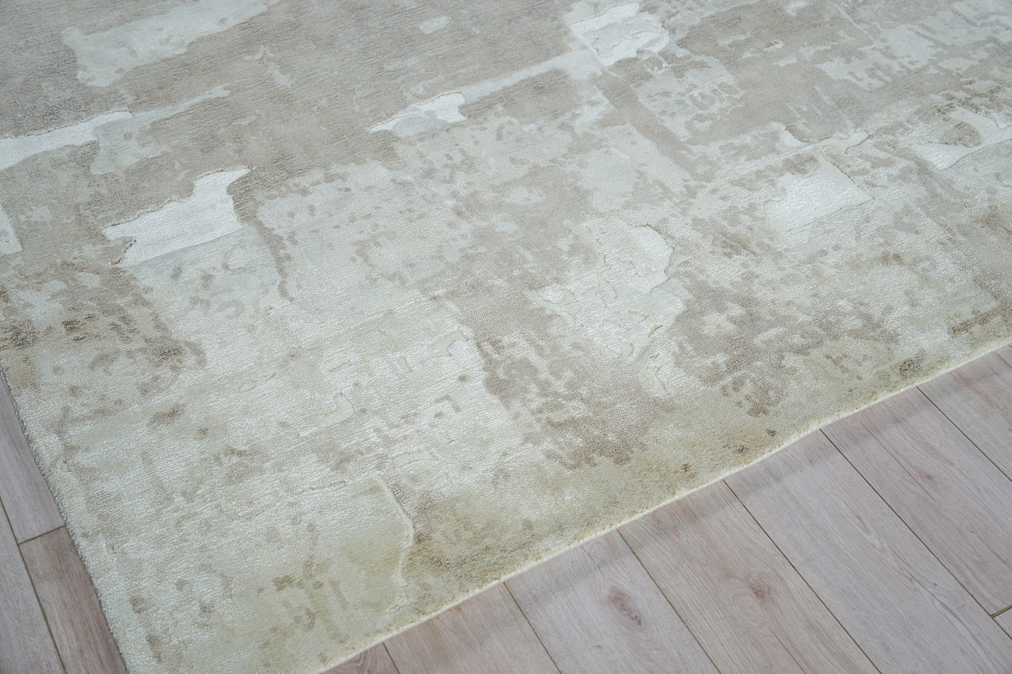 Cream-beige distressed area rug on light wood floor, hand loomed.