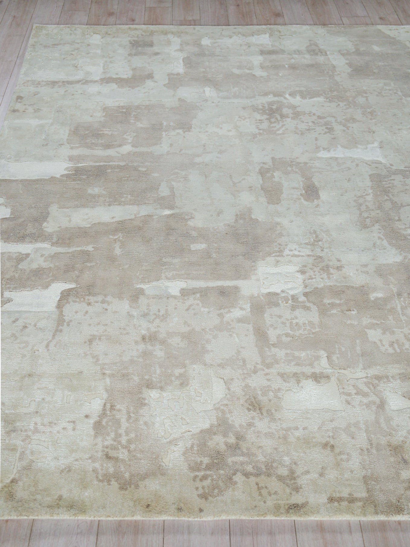 Neutral cream and beige distressed area rug with patchwork pattern on light wooden floor.