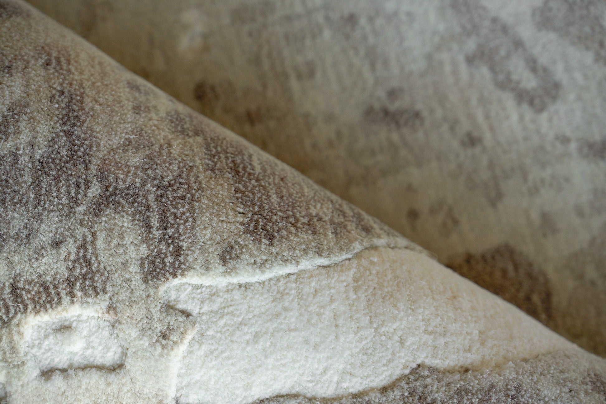 Soft, plush brown-beige rug with a mottled pattern and a folded edge.