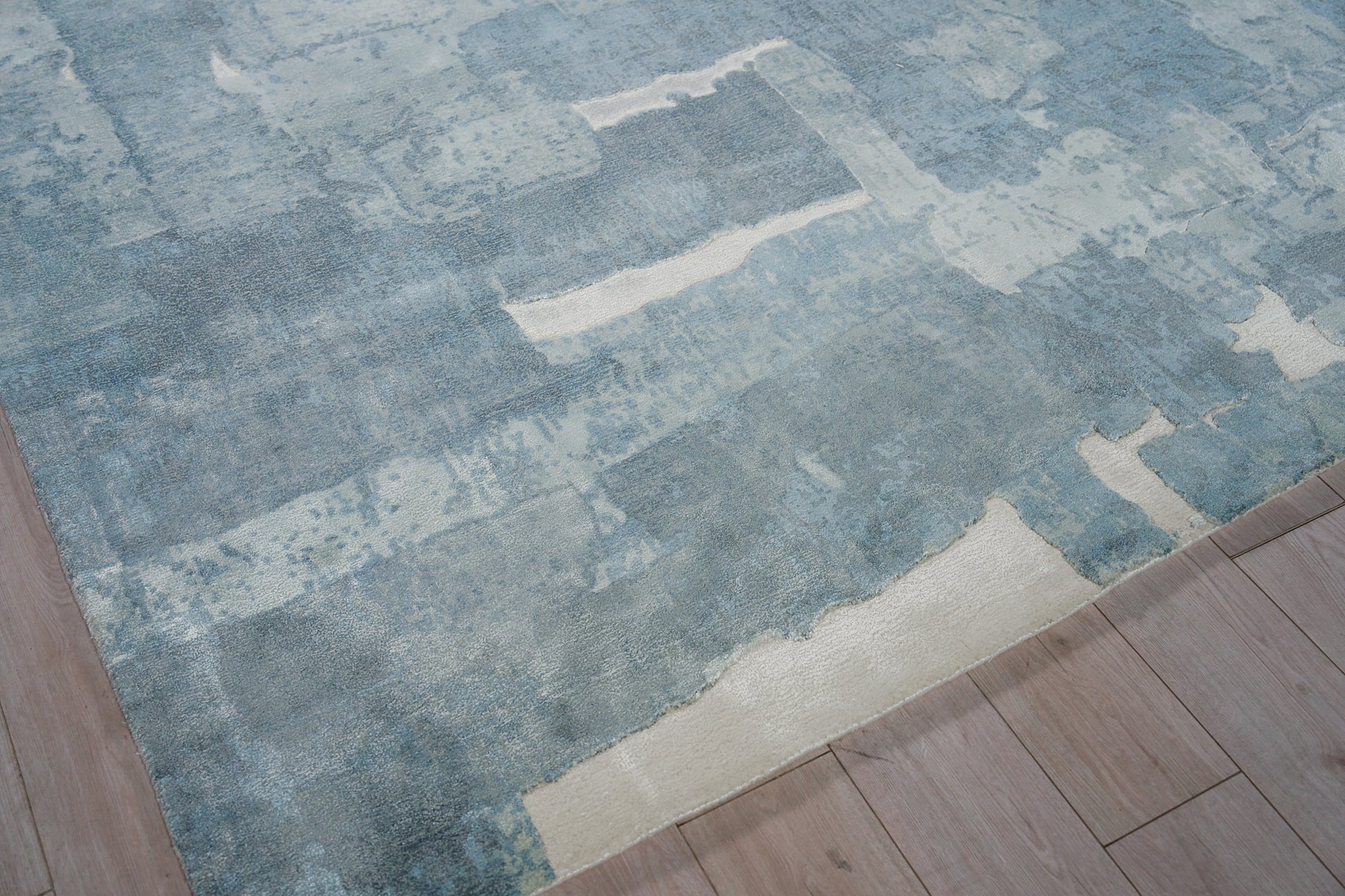 Blue abstract patterned area rug with a beige border on a wooden floor.