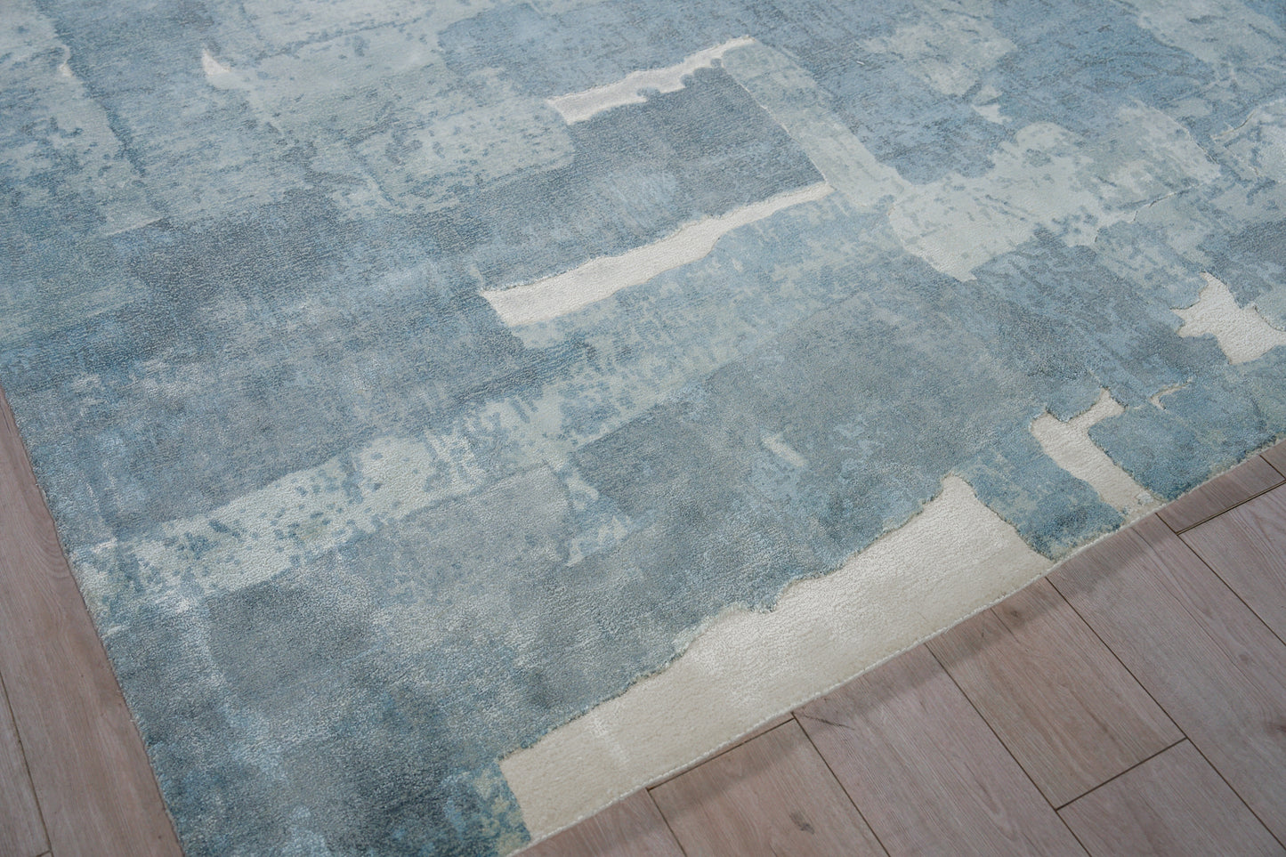 Blue abstract area rug with varied blue hues and cream accents on light wood flooring.