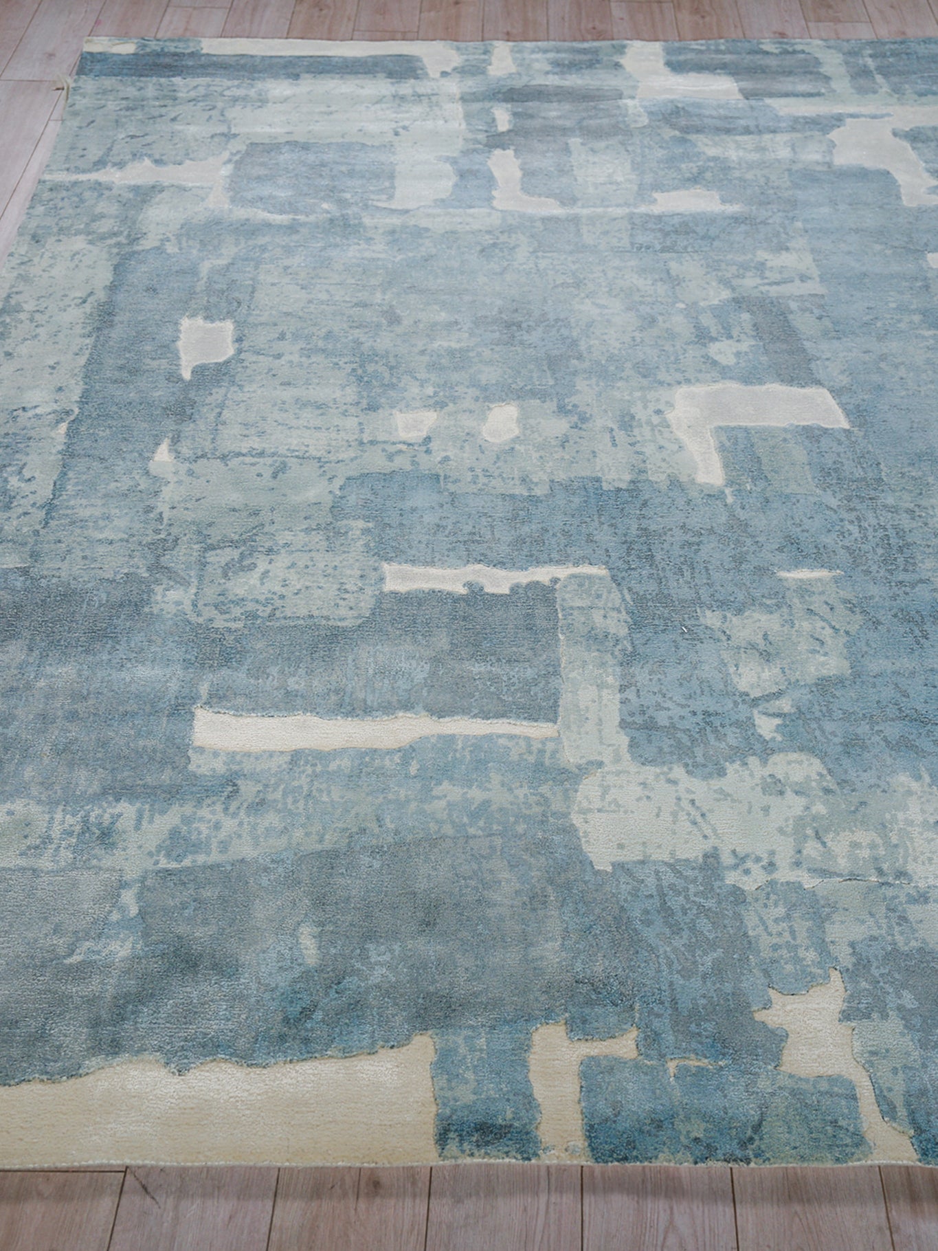 Blue distressed patchwork area rug with cream patches, modern abstract pattern on a wood floor.