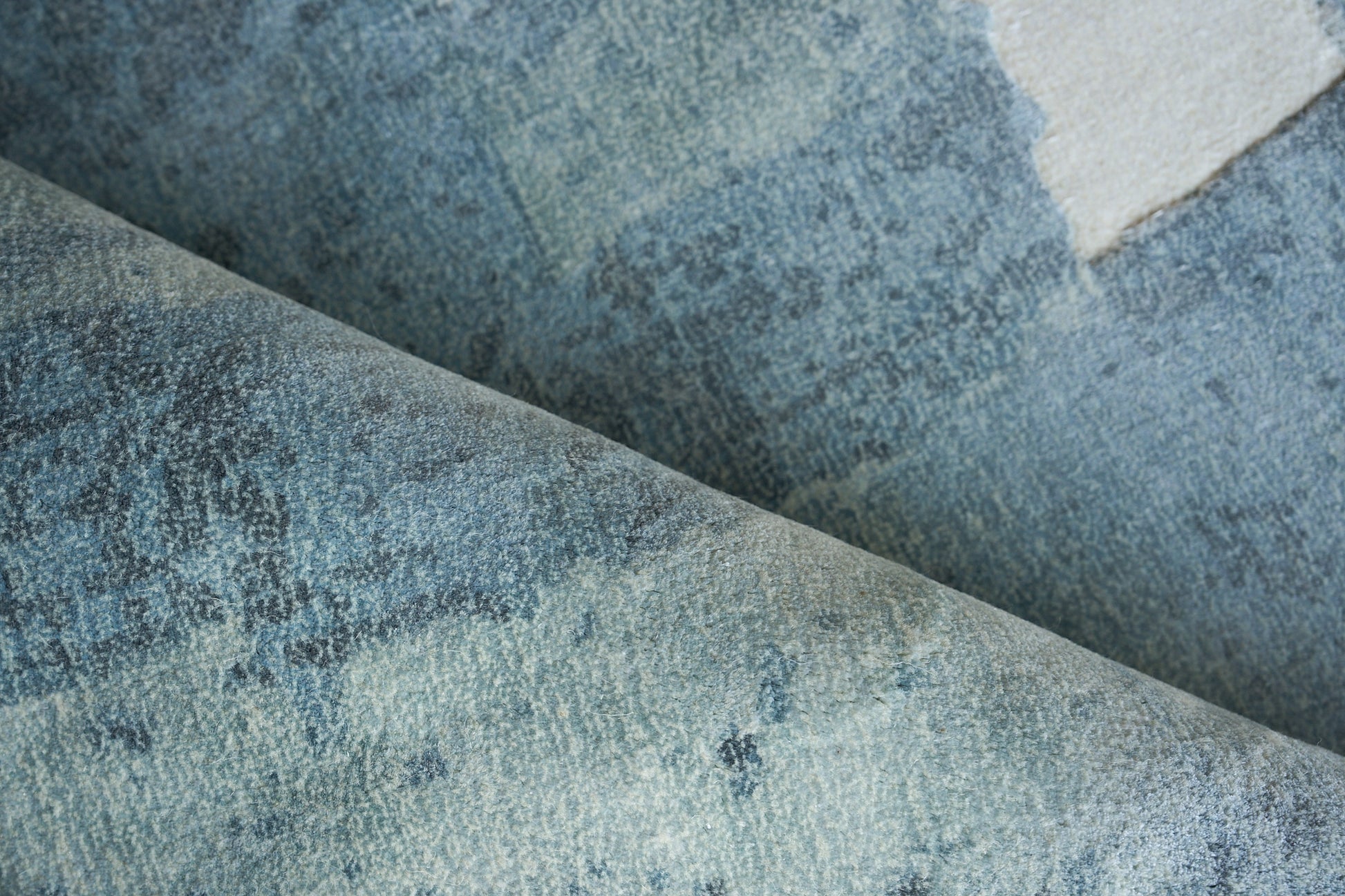 Blue denim-style rug with faded patches, folded to reveal a soft, textured weave; hand loomed.