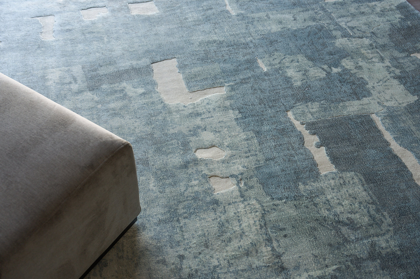 Blue distressed area rug with pale beige patches under a gray upholstered sofa.