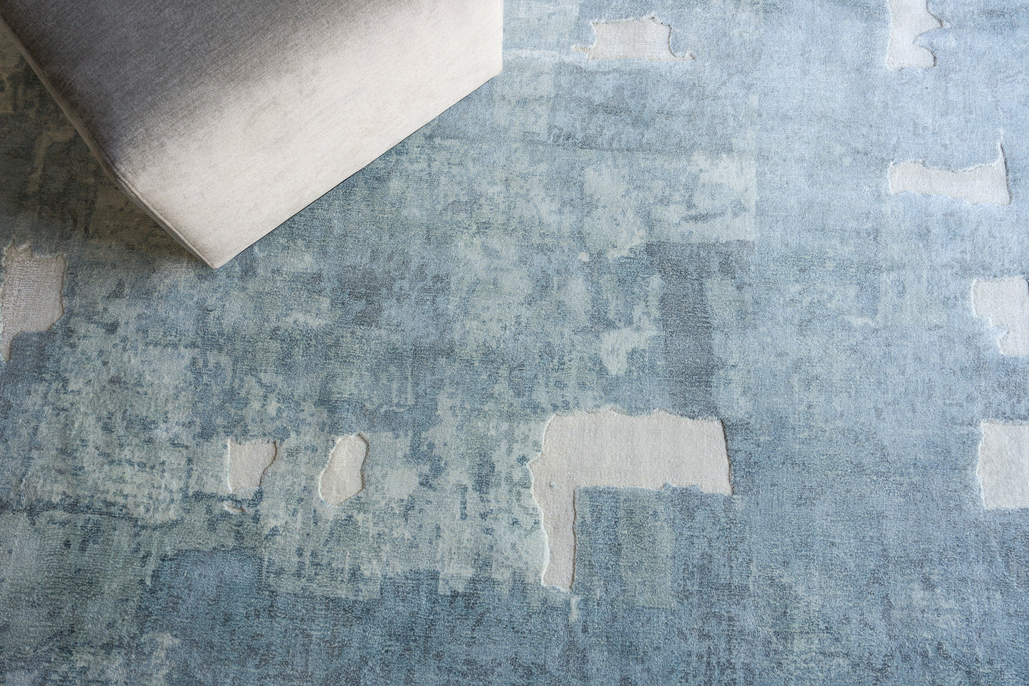 Blue distressed area rug with lighter rectangular patches; corner of light gray sofa visible.