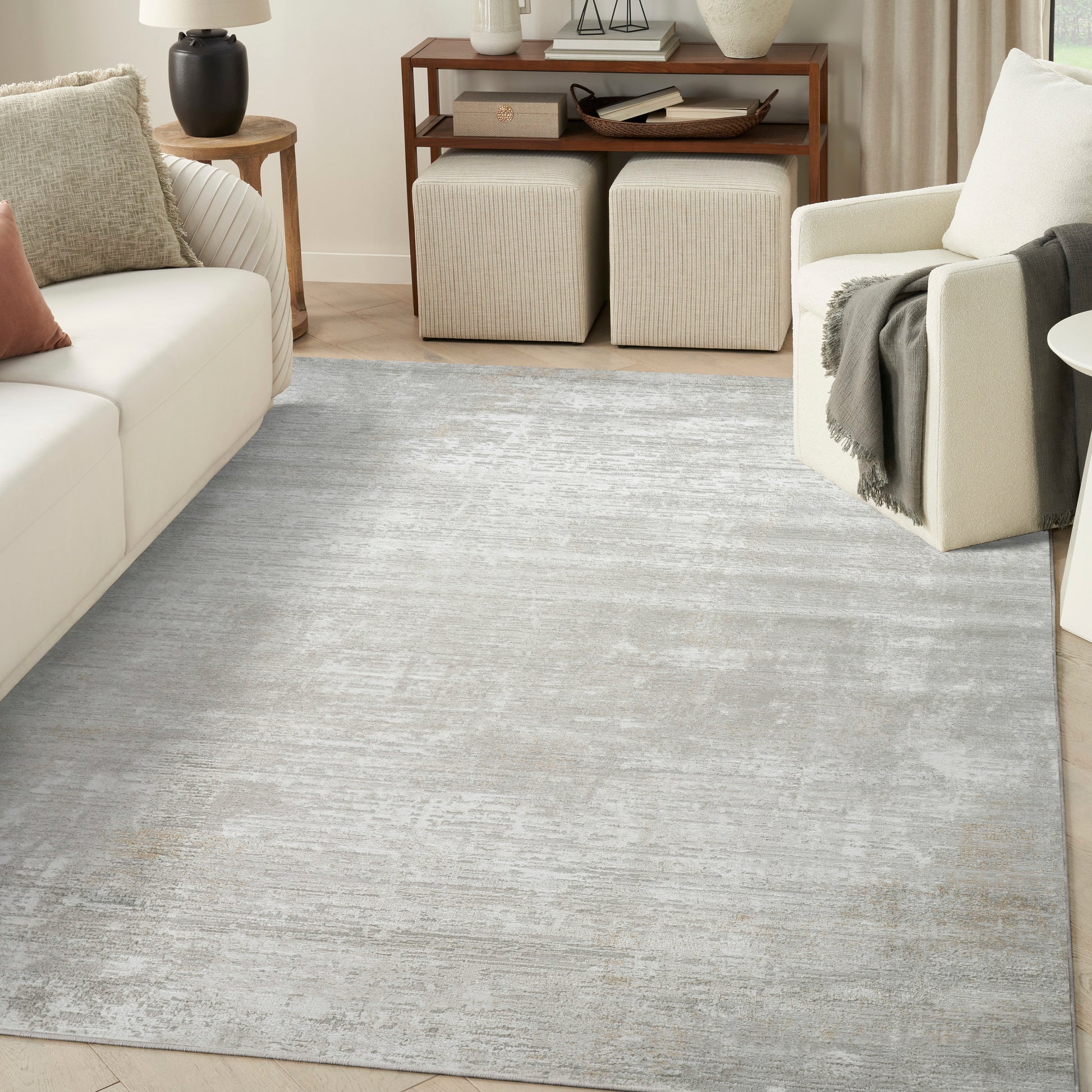 Soft gray distressed area rug in a modern living room with cream sofa, beige ottomans & wooden console table.