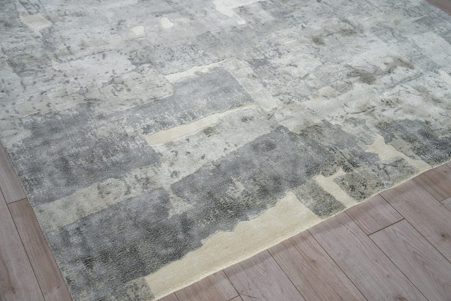 Rectangular area rug in muted grey, beige and cream with a distressed abstract block pattern on a wooden floor.