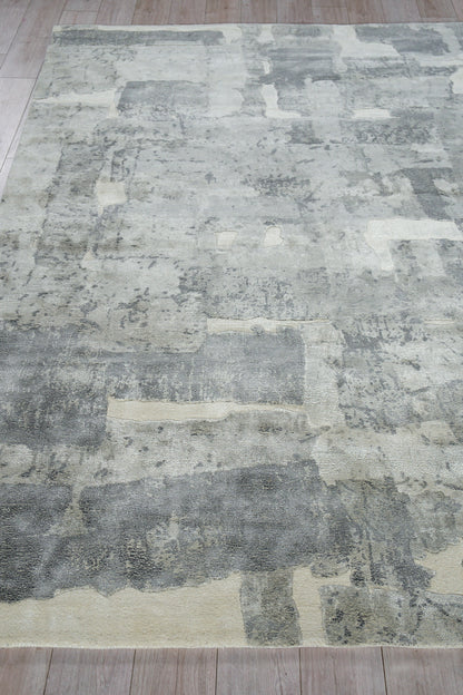 Grey and ivory abstract patchwork area rug with distressed pattern on light wood floor.