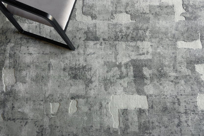 Gray textured rug with irregular lighter patches, seen with a black metal-framed chair in the corner.