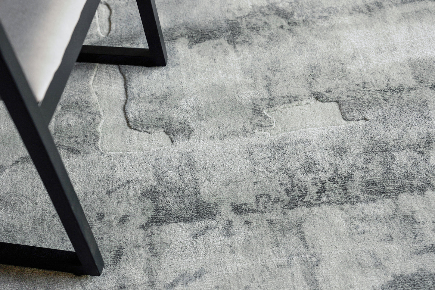 Gray distressed-pattern area rug with marble-like patches and a black metal chair leg resting on it.
