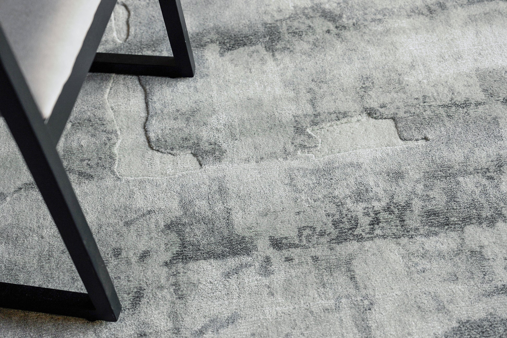Gray distressed-pattern area rug with marble-like patches and a black metal chair leg resting on it.