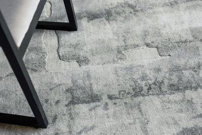 Gray distressed-pattern area rug with marble-like patches and a black metal chair leg resting on it.