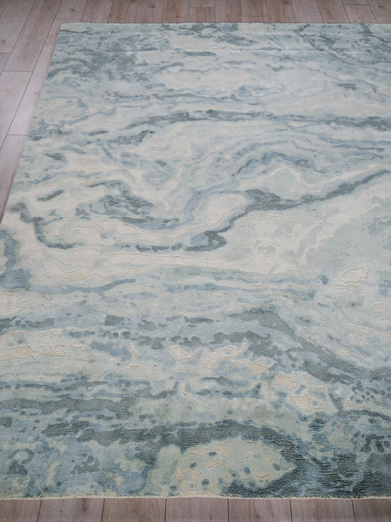 Large rectangular rug with pale blue, ivory and gray marble-like pattern; modern abstract style on wood floor.