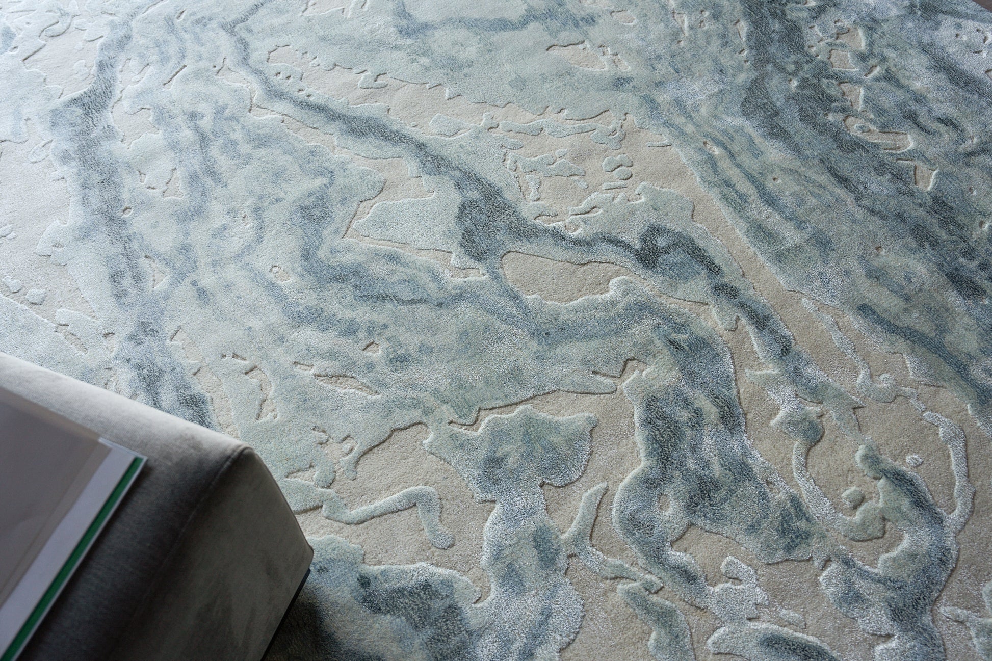 Abstract blue and beige rug with flowing river-like patterns; corner of gray sofa visible.