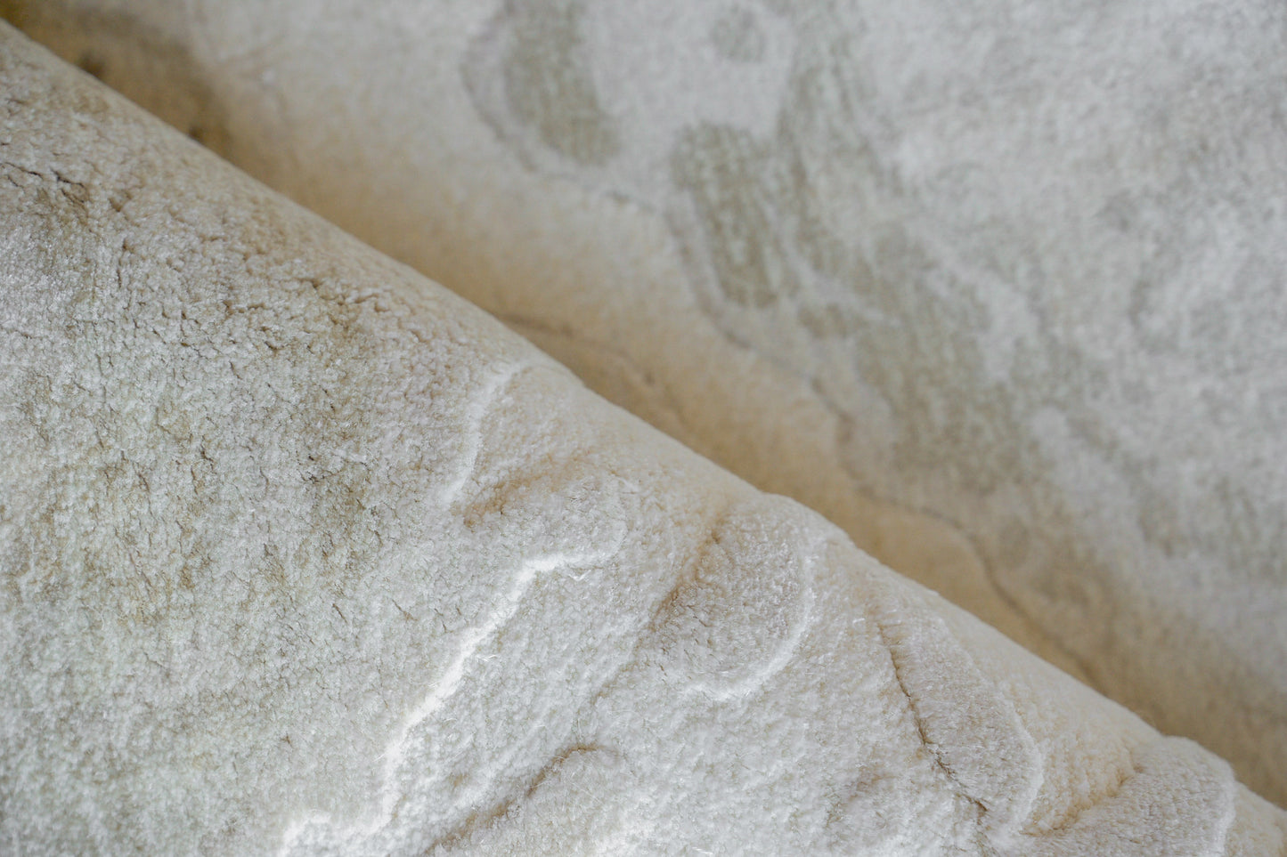 Close-up of a pale white rug with soft gray veining and a textured, wrinkled surface; indoor hand-loomed rug.