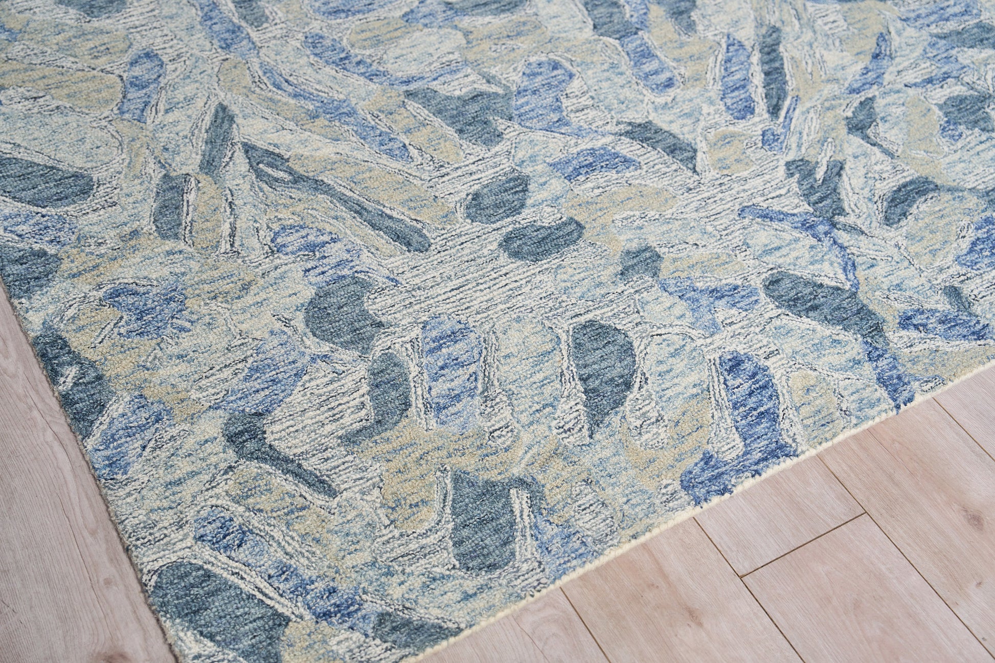 Blue-toned abstract rug with cream and beige stone-like shapes on light wood flooring.