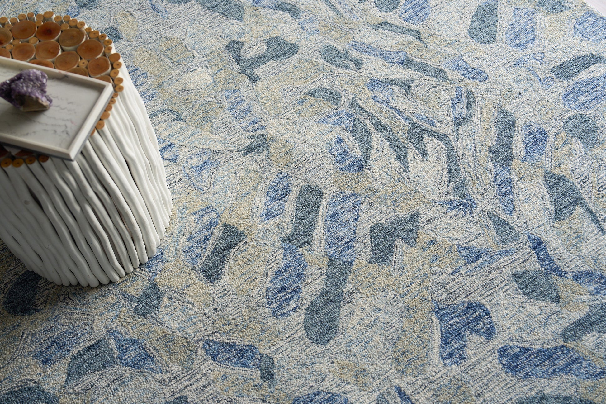 Blue & beige abstract area rug with textured pile; white ribbed round side table & marble tray & amethyst cluster.