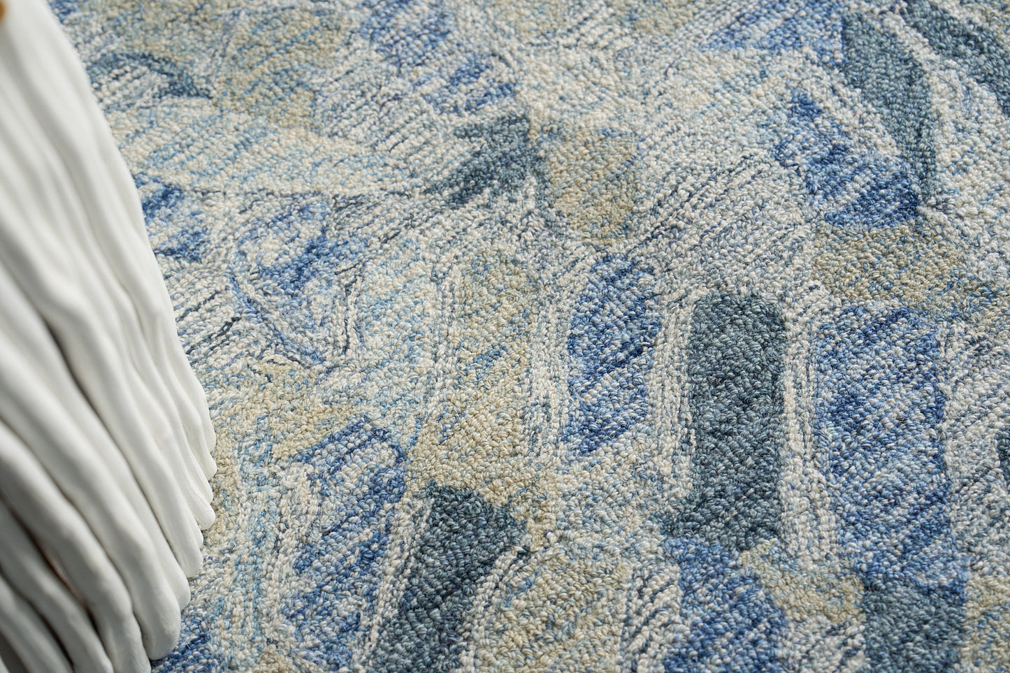 Blue and beige textured rug with abstract shapes; plush loop pile and a white pleated fabric edge visible.