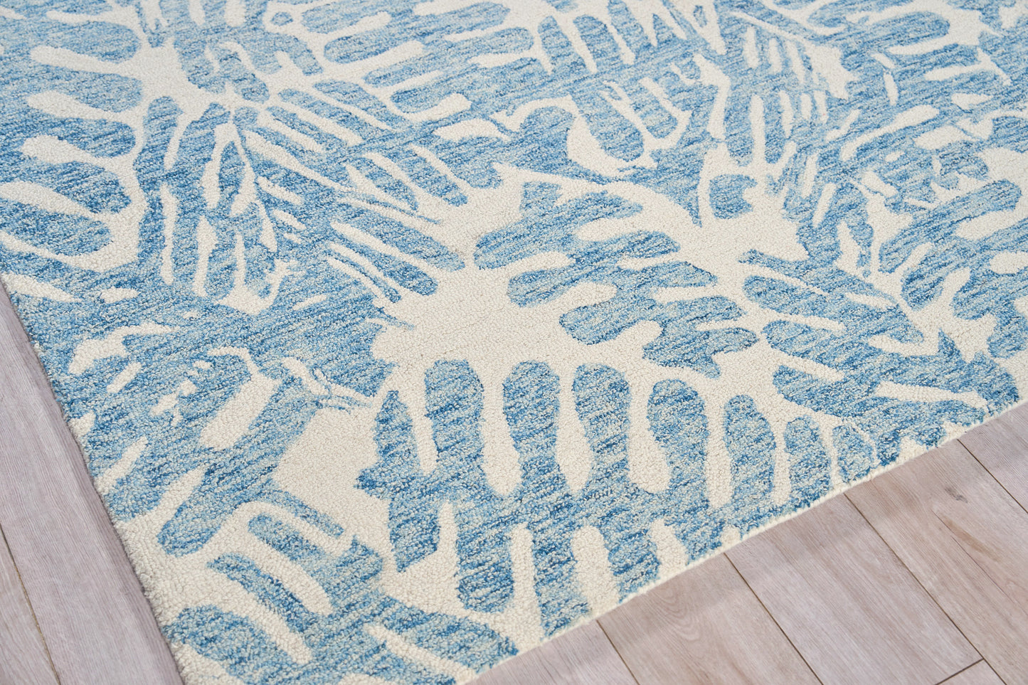 Blue and ivory hand-tufted rug with an abstract coral-like pattern and plush texture on light wood floor.
