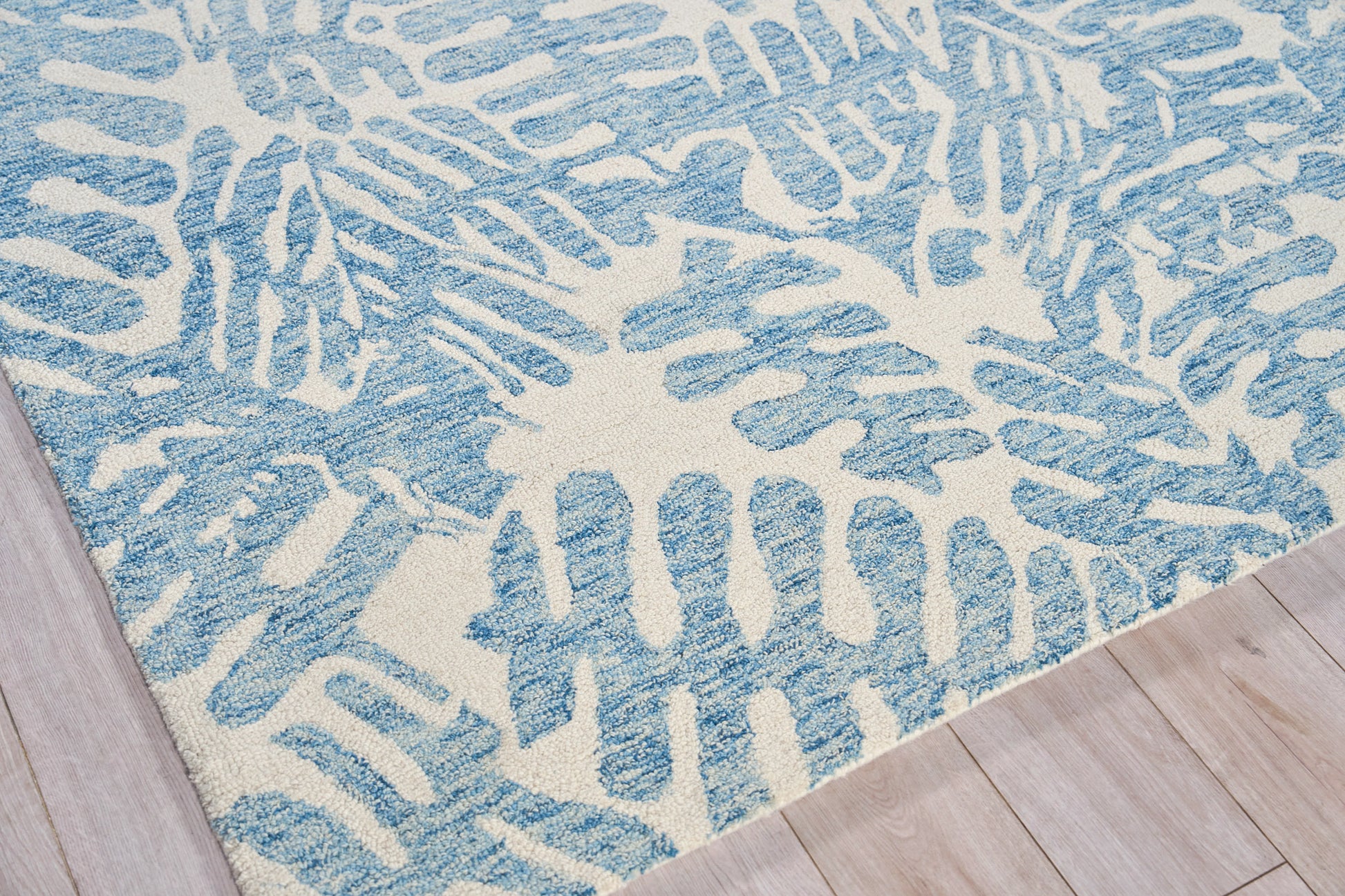 Blue and ivory hand-tufted rug with an abstract coral-like pattern and plush texture on light wood floor.