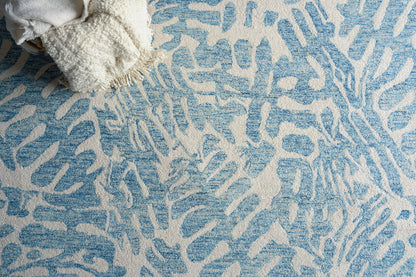 White rug with blue abstract pattern and a cream chunky throw draped at the corner.