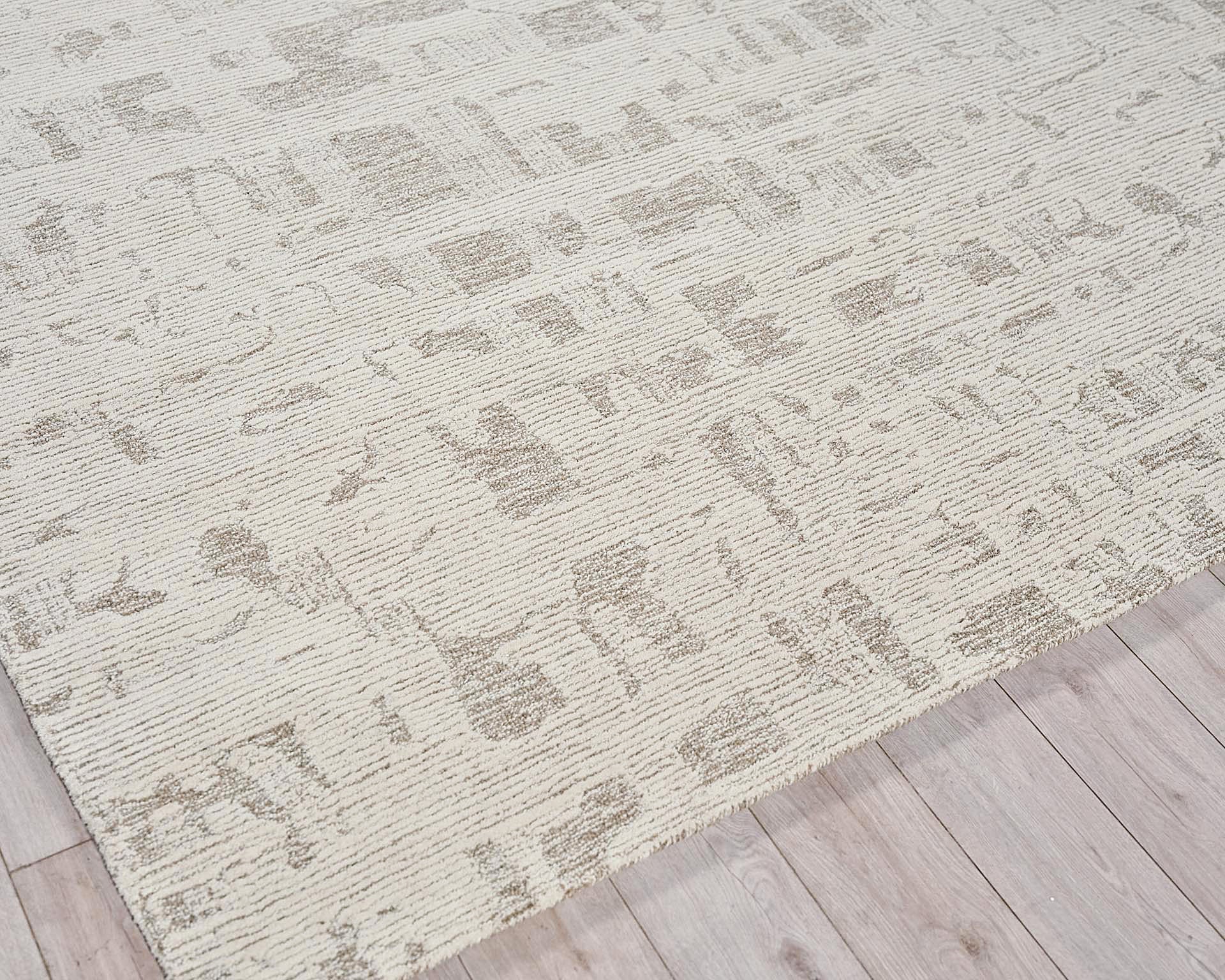 Cream low-pile area rug with a muted taupe abstract pattern on a light wood floor.