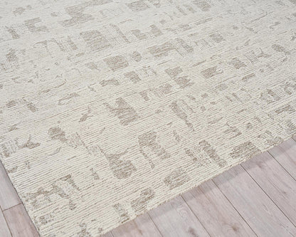 Cream low-pile area rug with a muted taupe abstract pattern on a light wood floor.