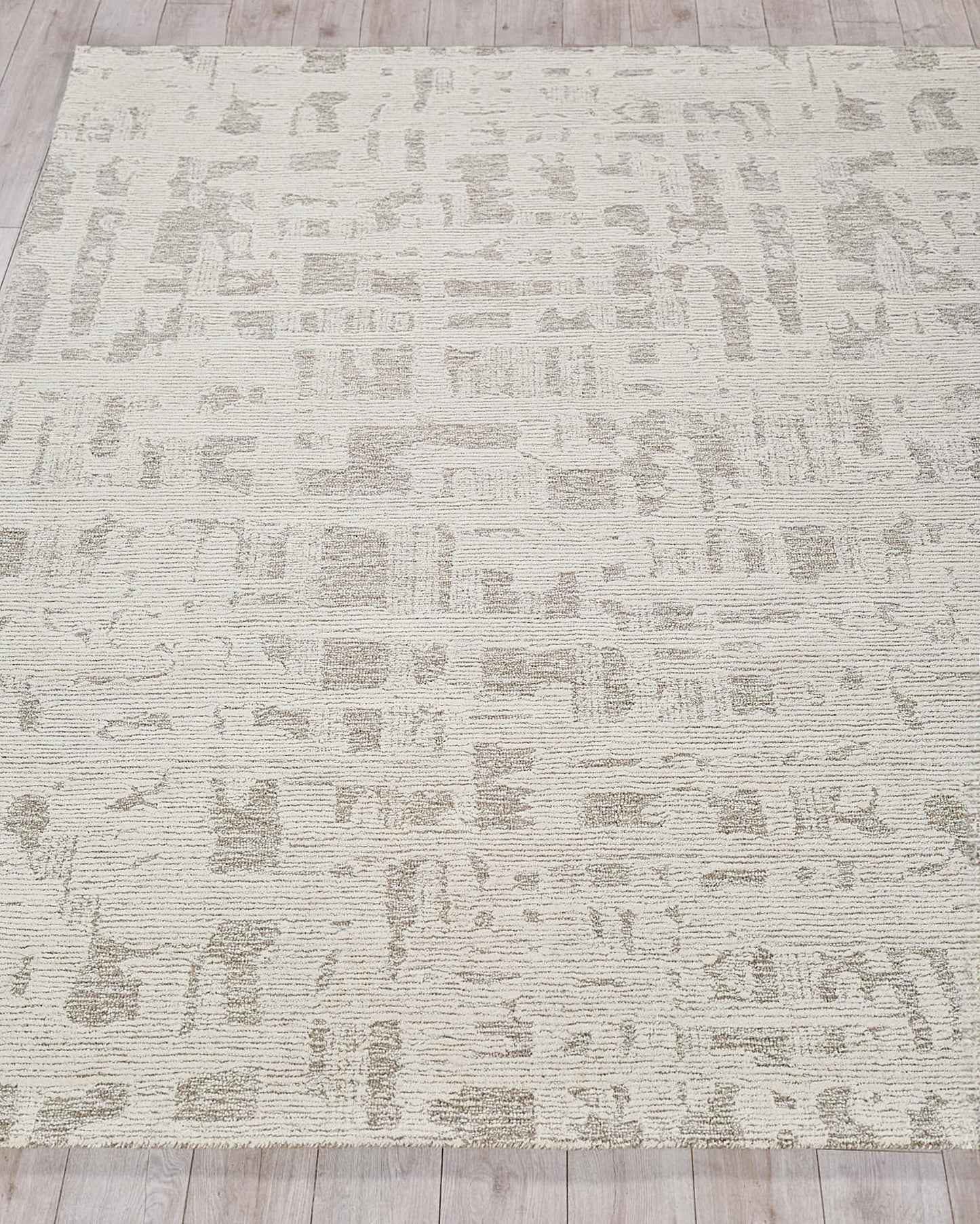 Beige area rug with abstract taupe pattern, textured loop pile, on light wood floor