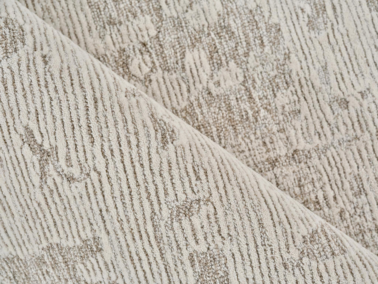 Beige textured rug close-up with subtle damask pattern and soft pile; folded edge visible.