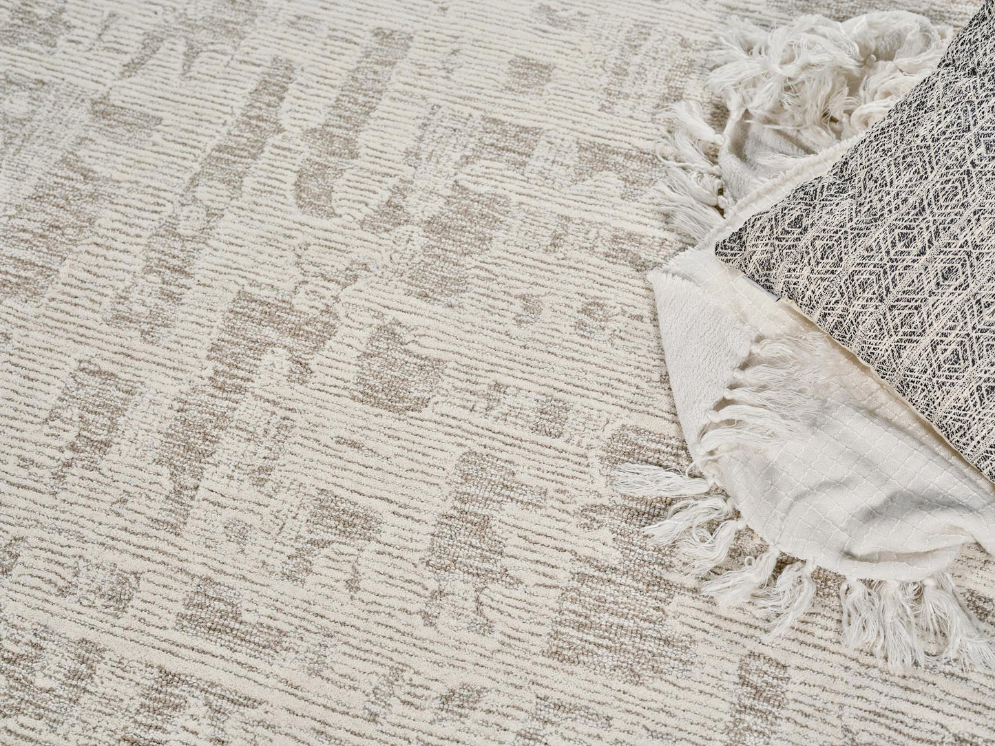 Beige geometric rug with tassel fringe along edge, paired with a folded light woven throw.