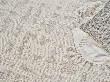 Beige geometric rug with tassel fringe along edge, paired with a folded light woven throw.