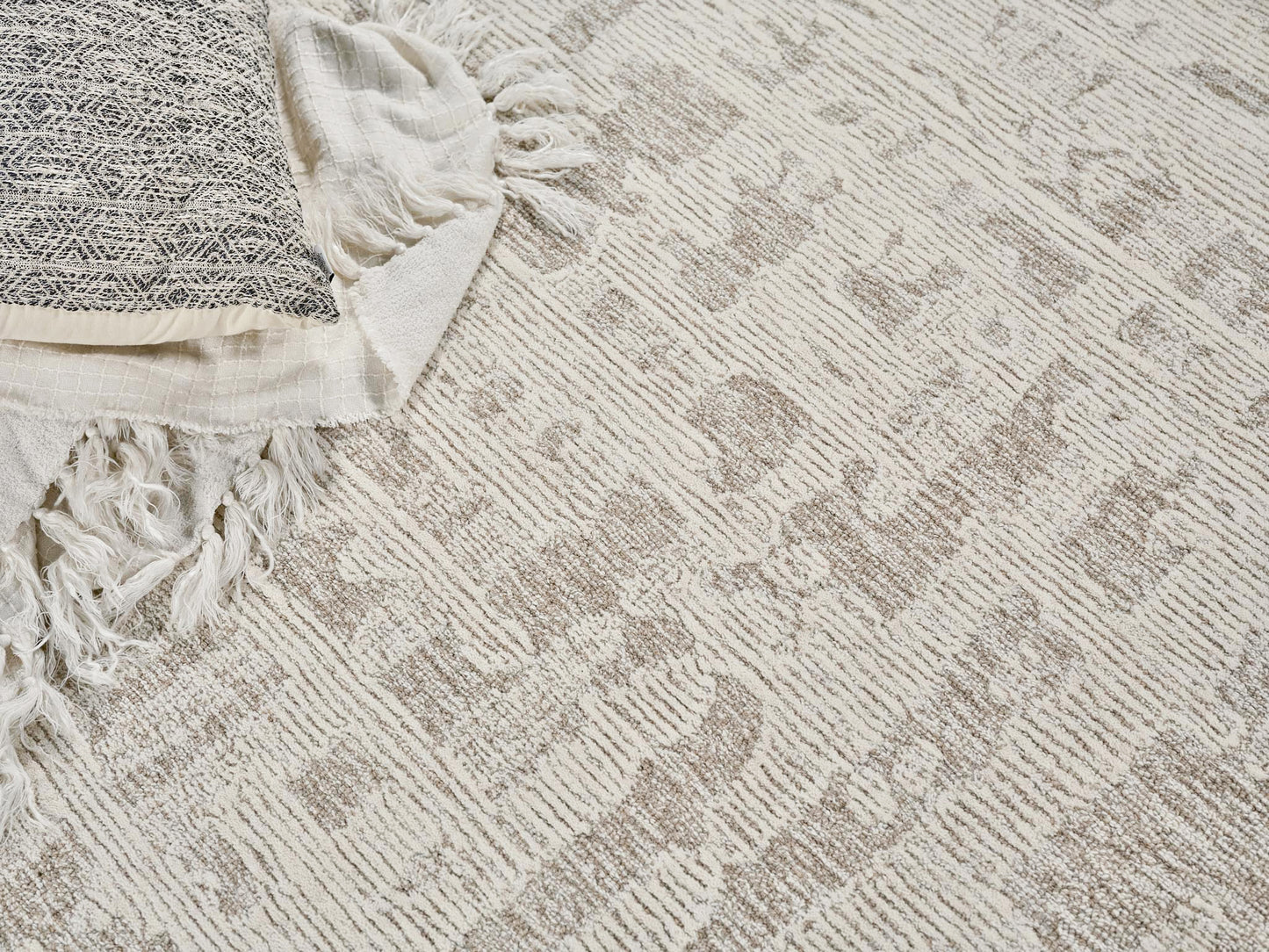 Cream and taupe patterned woven area rug with fringed edge, paired with a white textured throw blanket.