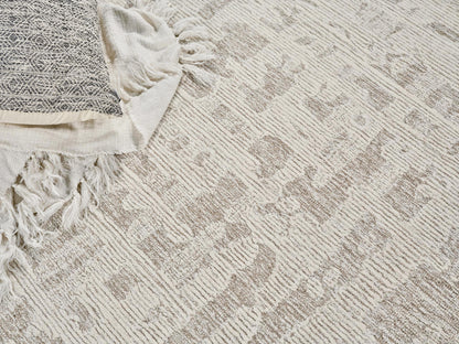 Cream and taupe patterned woven area rug with fringed edge, paired with a white textured throw blanket.