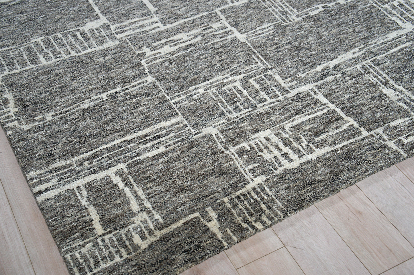 Gray area rug with white geometric line pattern on light wood floor; modern rectangular shapes.