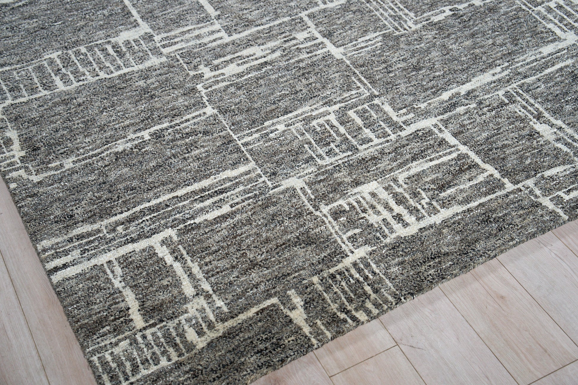 Gray area rug with white geometric line pattern on light wood floor; modern rectangular shapes.