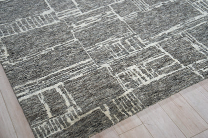 Gray area rug with white geometric line pattern on light wood floor; modern rectangular shapes.