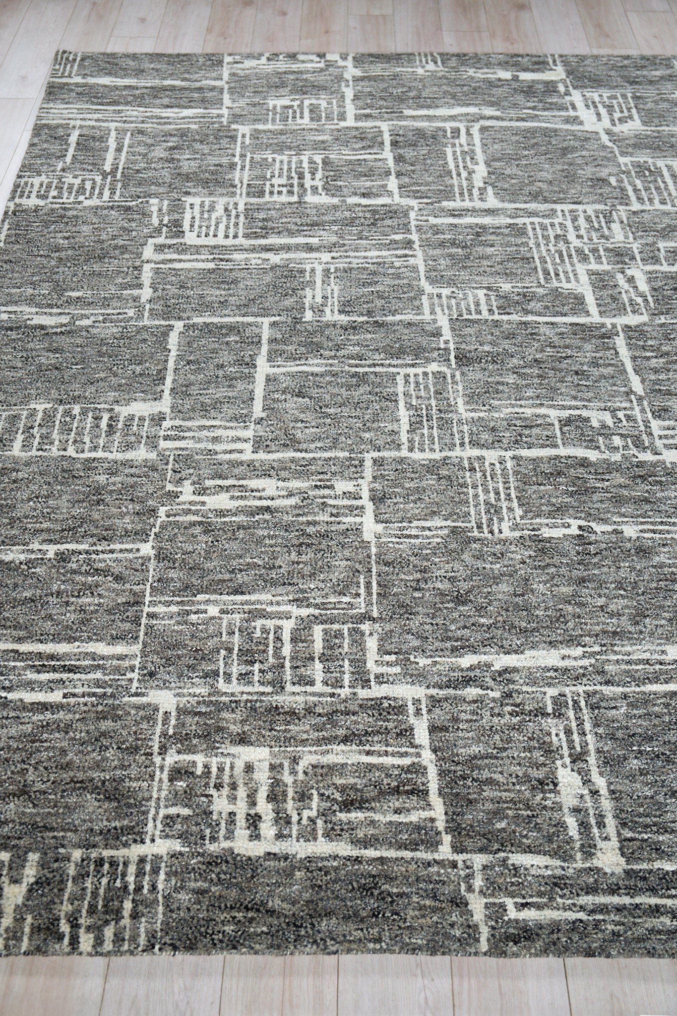 Gray geometric area rug with cream rectangular patterns and textured pile, modern look on light wood floor.