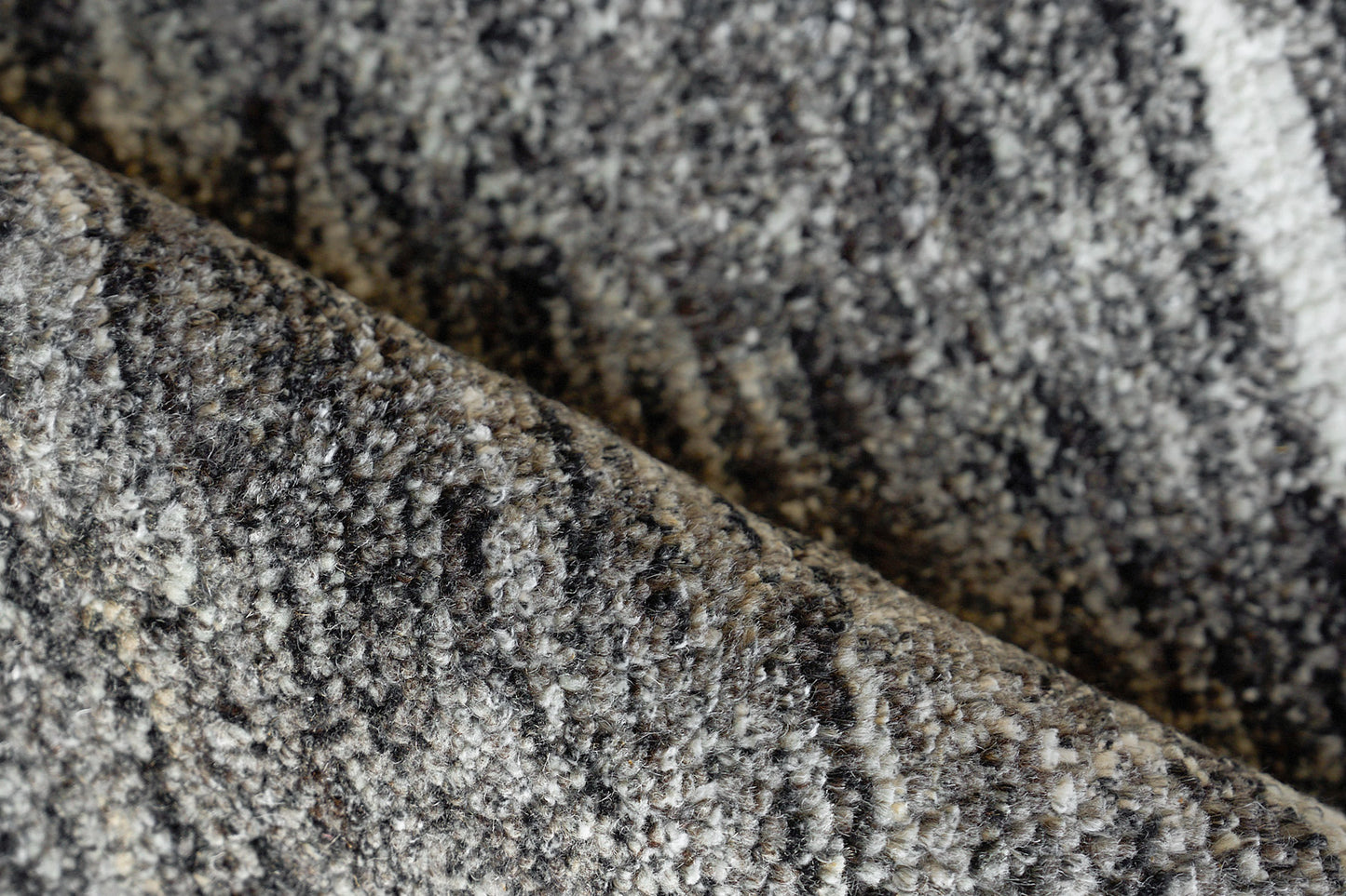 Close-up of a gray speckled rug with black, white and taupe hues; soft loop-pile texture.