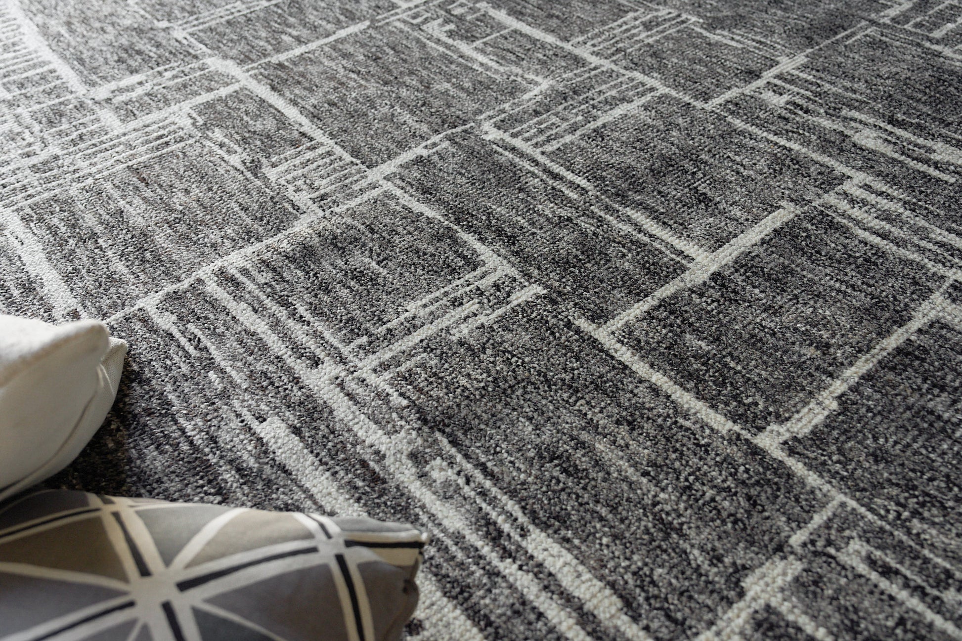 Gray geometric area rug with a white linear pattern; soft textured fibers, near decorative cushions.
