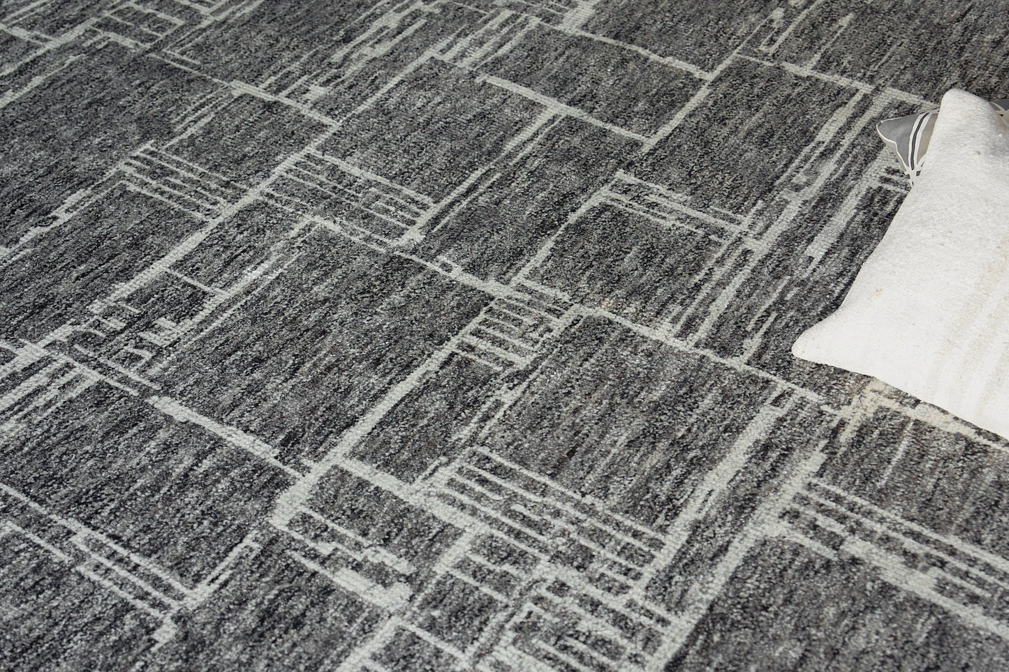 Gray textured rug with a white geometric grid pattern; modern rectangular lines, edge shows a light cream pillow.