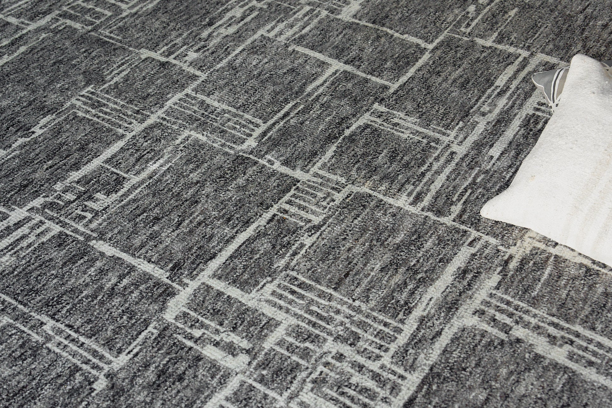 Gray textured rug with a white geometric grid pattern; modern rectangular lines, edge shows a light cream pillow.