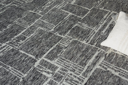 Gray textured rug with a white geometric grid pattern; modern rectangular lines, edge shows a light cream pillow.