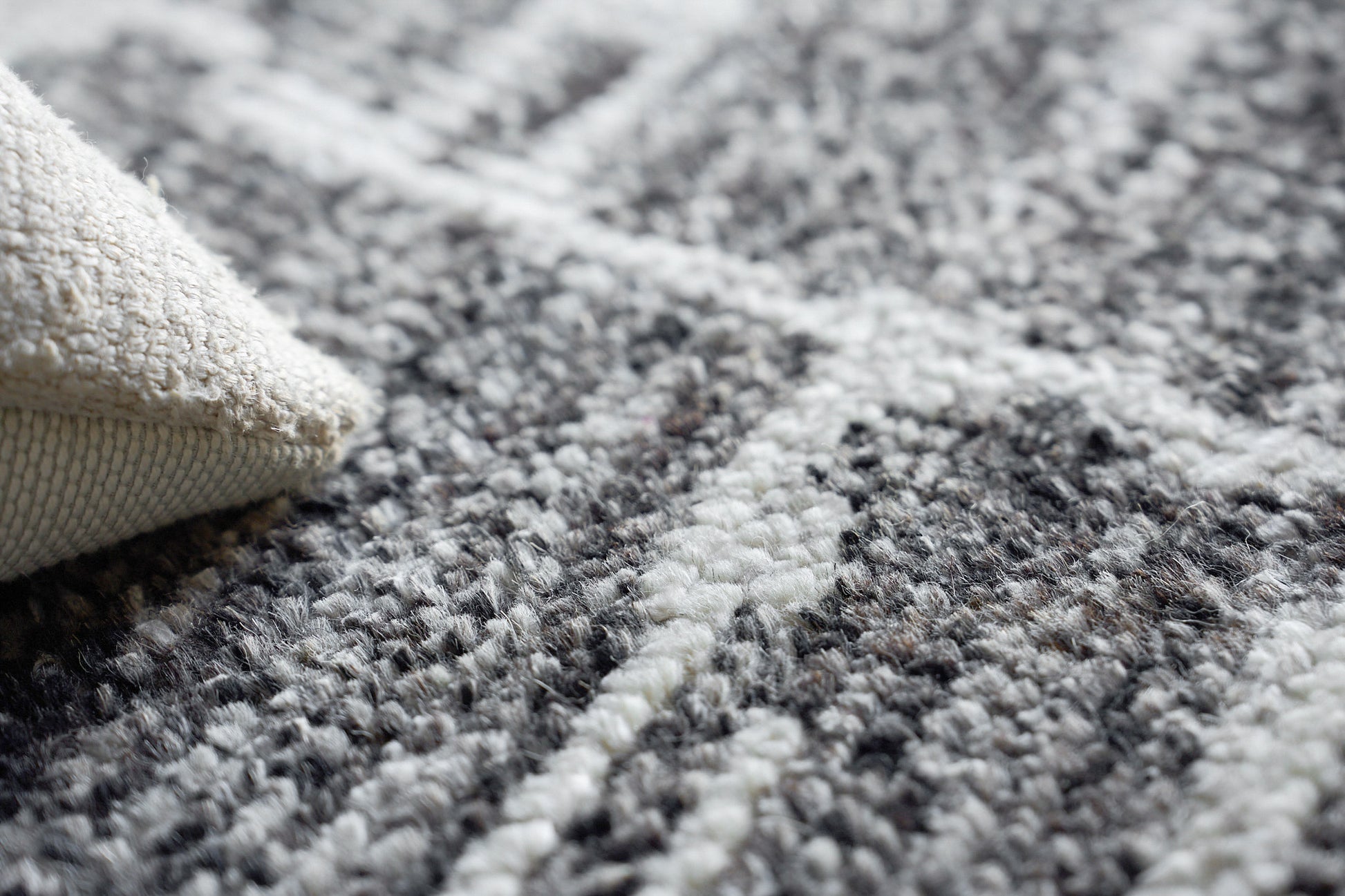 Close-up of a hand-knotted indoor rug in gray, black and ivory with a beige backing.